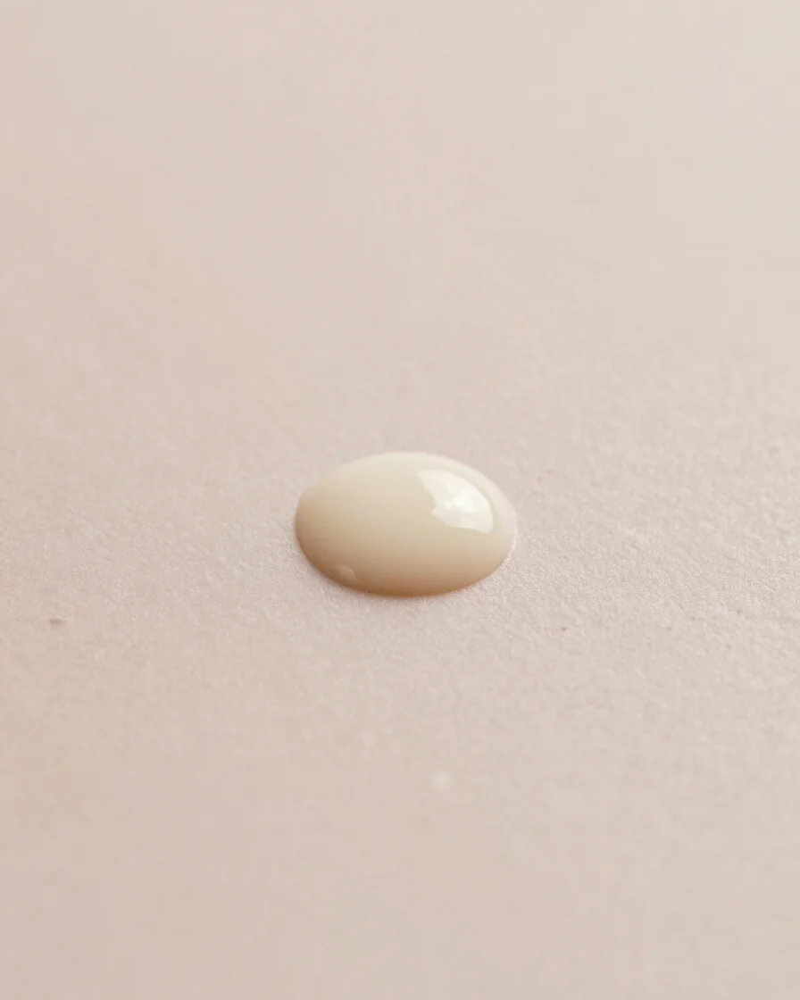 Wide studio shot of a delicate cream droplet on a smooth alabaster surface, soft diffused light, blush and ivory tones,